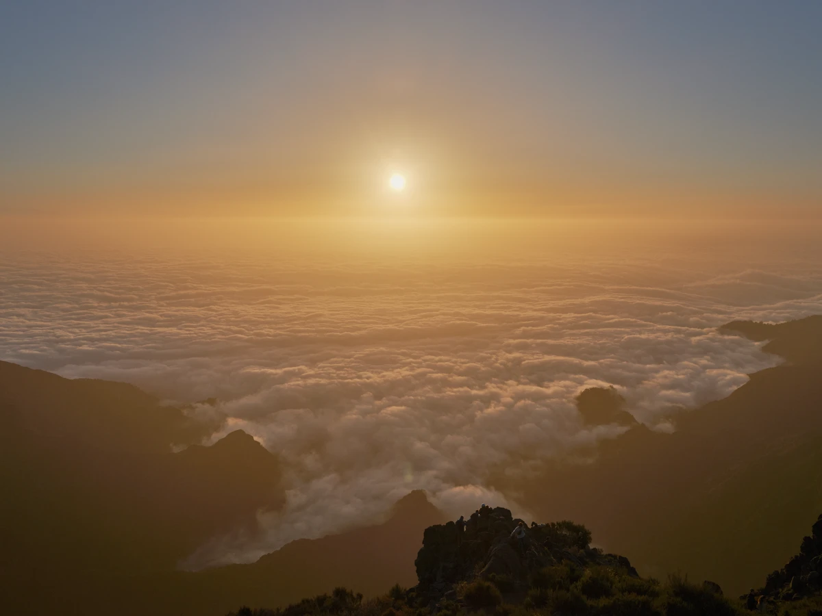 Lever de soleil à Pico do Areeiro, sur une mer de nuages, silhouettes de promeneurs sur un piton rocheux.